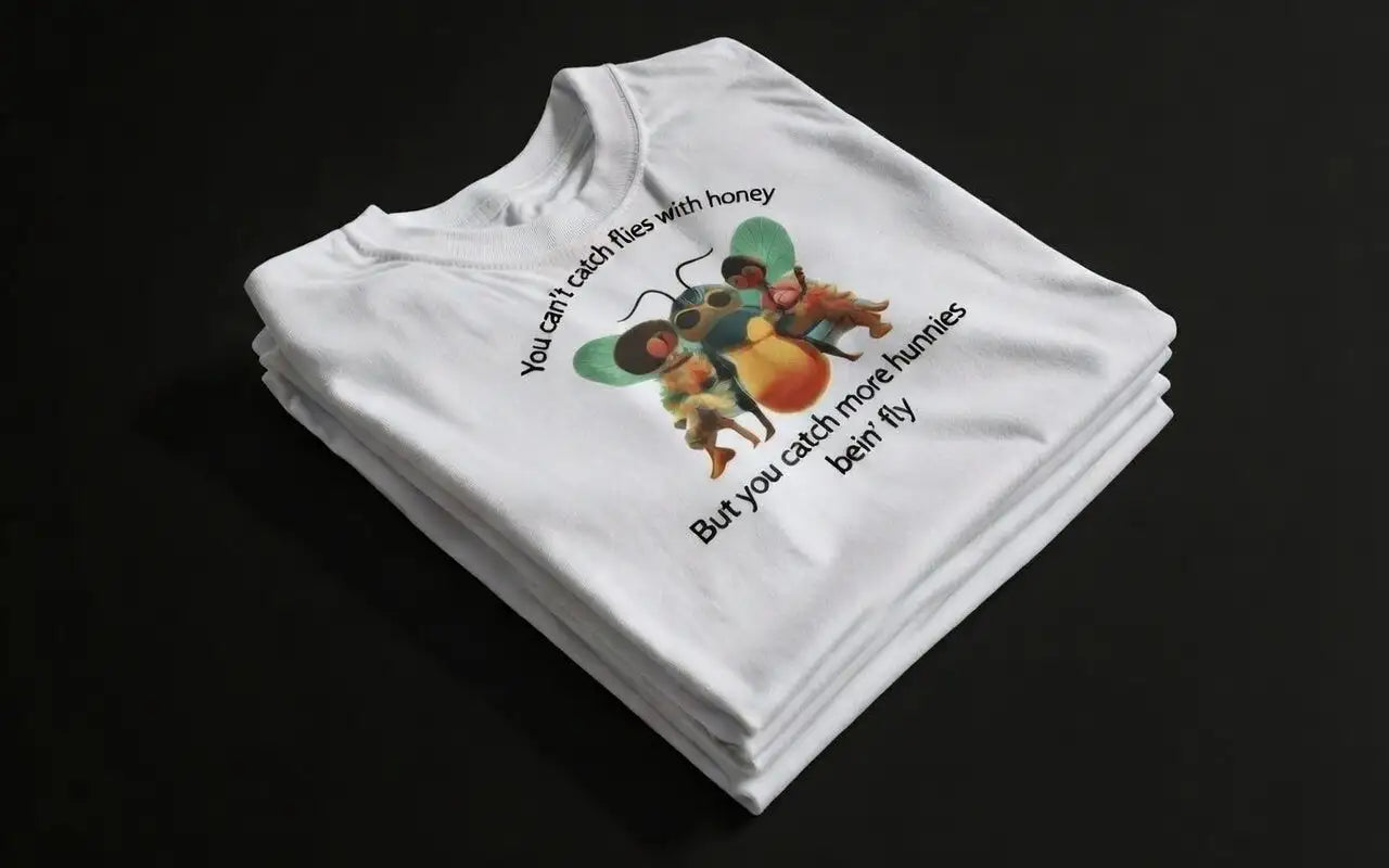 White cotton t-shirt featuring a colorful cartoon illustration of bees with sunglasses and the humorous text ’you can’t catch flies with honey / but you catch more hunnies bein’ fly.’
